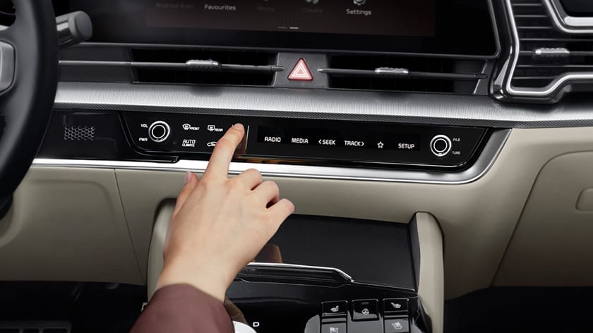 Una mano pulsa un botón en el panel de control central de un Kia Sportage