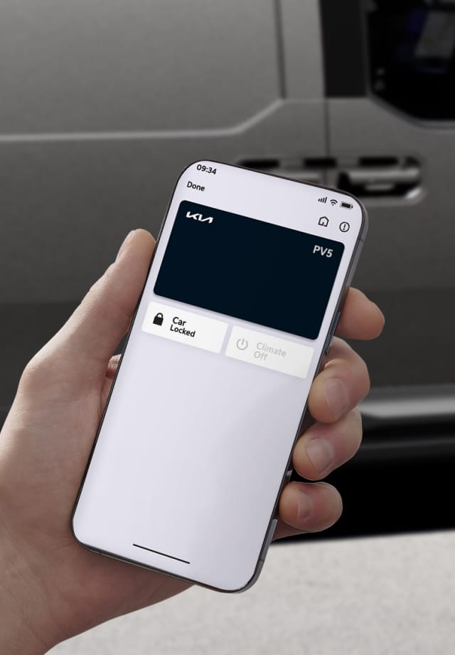 Hand holding a smartphone displaying a Kia PV5 digital key in front of the vehicle
