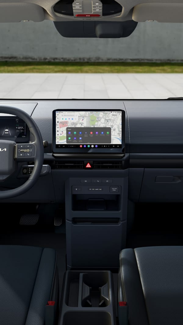 Vista delantera del área del conductor del interior del Kia PV5 que muestra el volante y la pantalla de infoentretenimiento