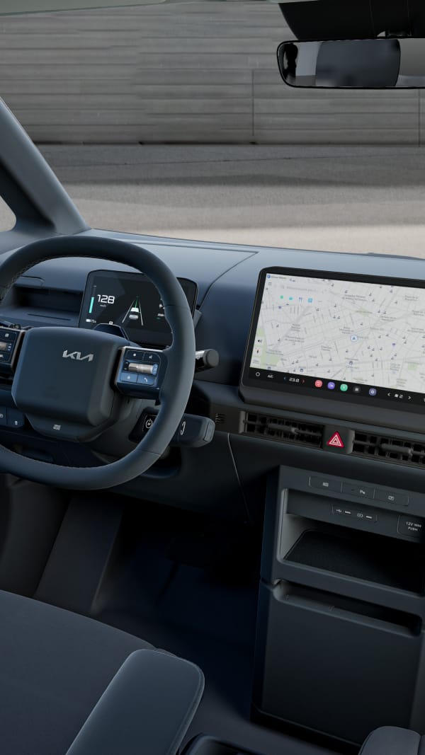 Angled interior view of the Kia PV5 cockpit showing the driver's seat, steering wheel and infotainment display