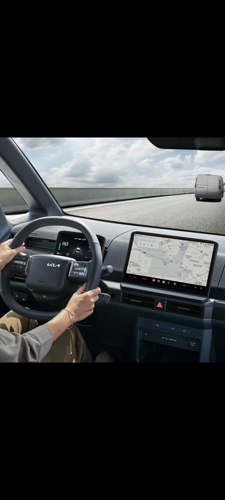 Driver holding steering wheel of the Kia PV5 Cargo with navigation screen visible