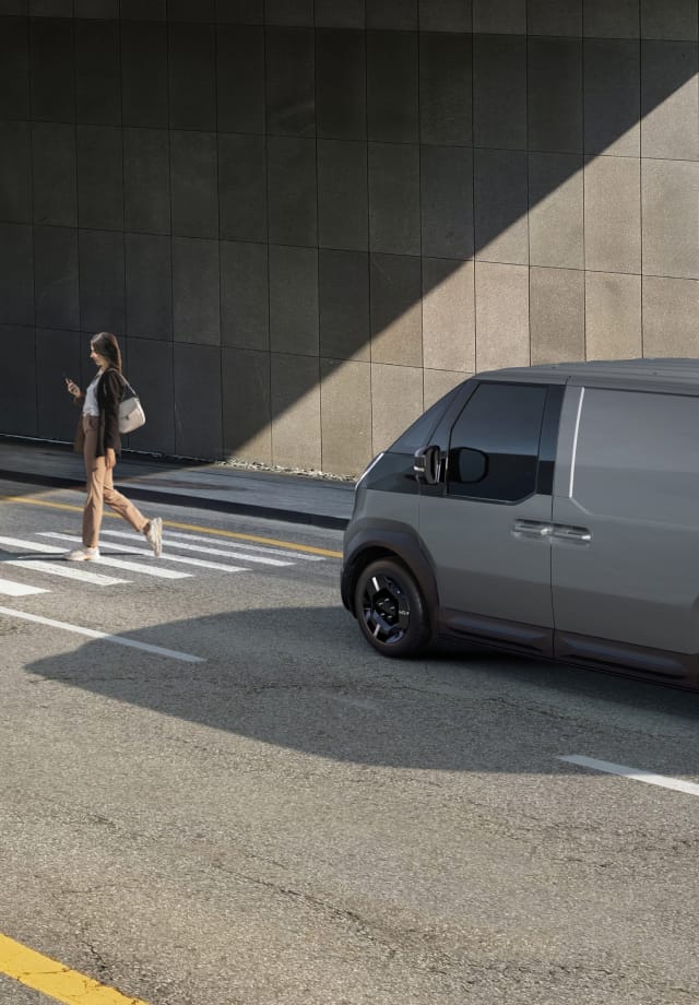 The Kia PV5 Cargo stopped at crosswalk while a pedestrian walks by