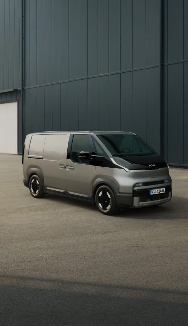 Rear view of the Kia PV5 Cargo charging with a man working on a laptop nearby
