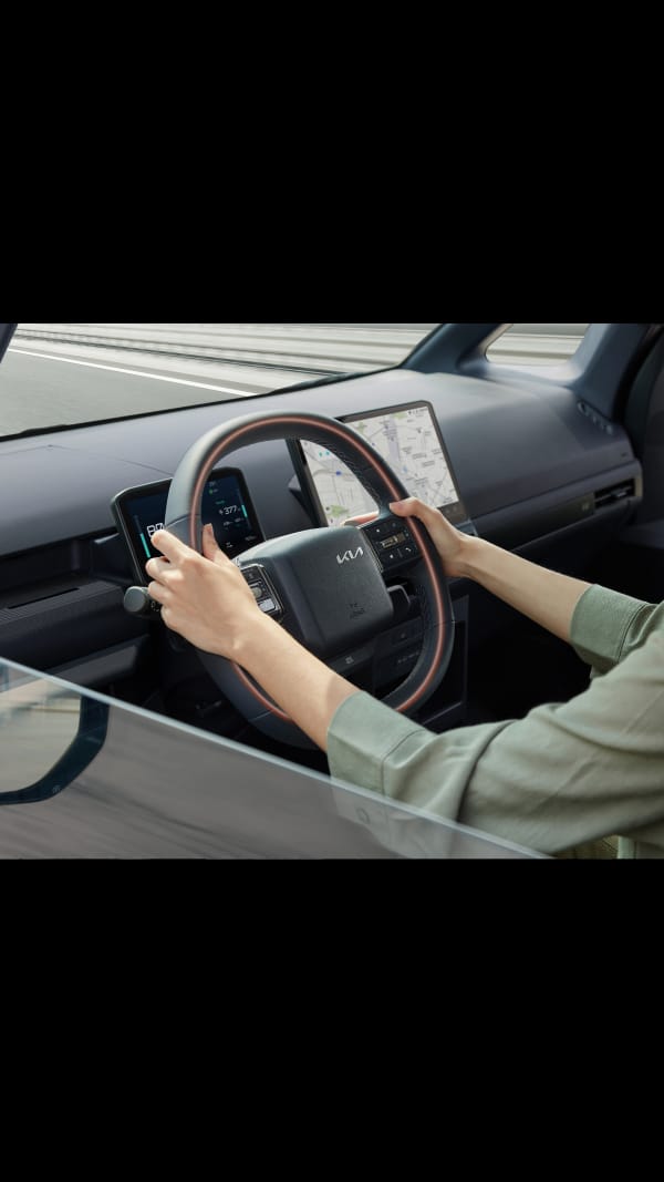 Close-up of the Kia PV5 Passenger steering wheel with driver’s hands