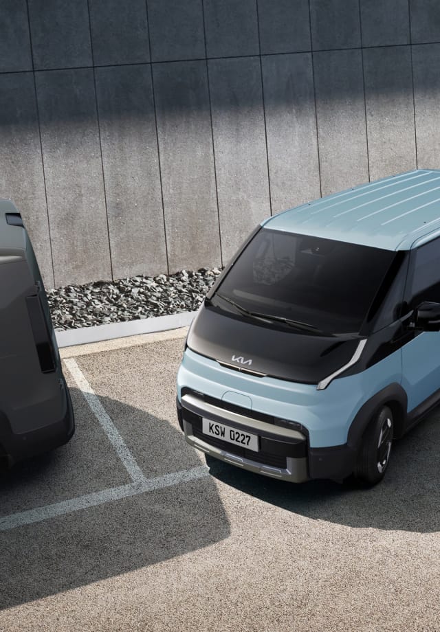 The Kia PV5 Passenger exiting a parallel parking space in a lot with two other vehicles