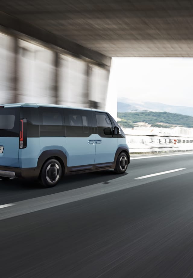 Rear view of the Kia PV5 Passenger driving on a highway with another vehicle ahead