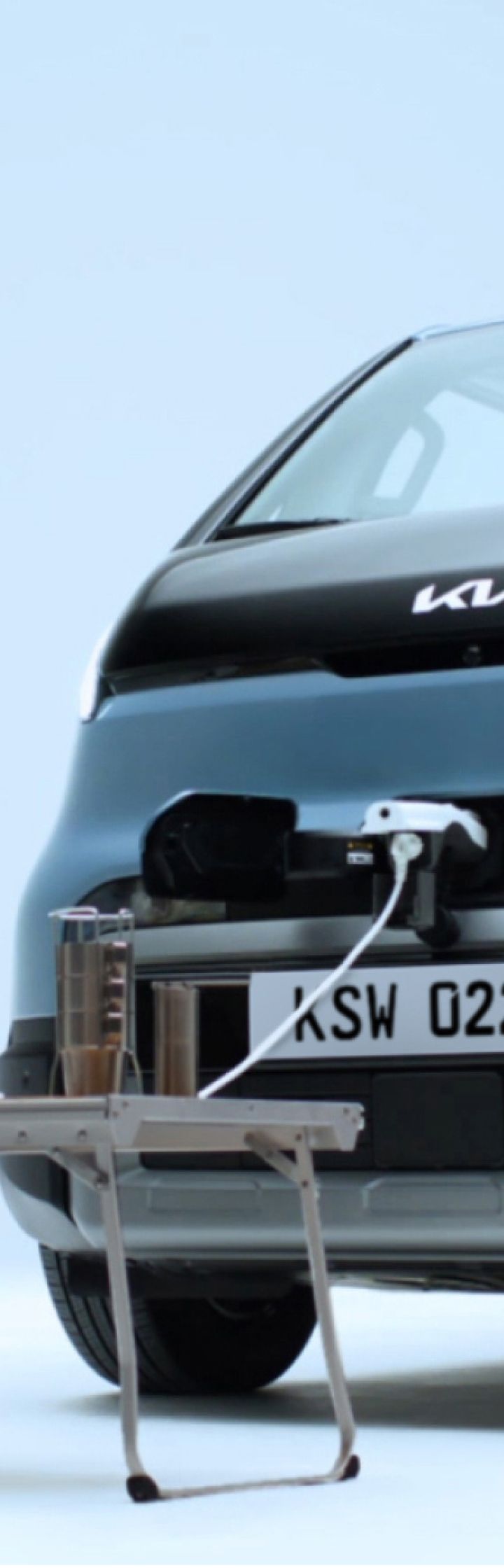 Rear view of the Kia PV5 Passenger charging with a man working on a laptop nearby