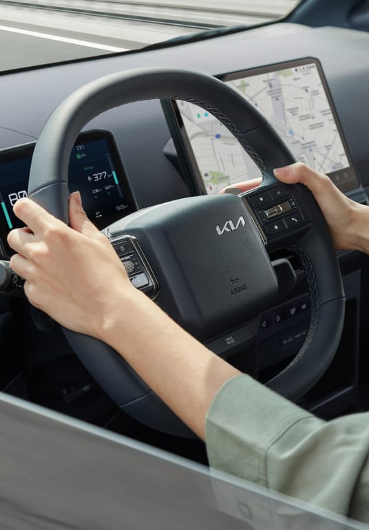 Fahrer hält das Lenkrad des Kia PV5 WAV – die Hands-on-Erkennung überwacht den Kontakt für mehr Fahrsicherheit.