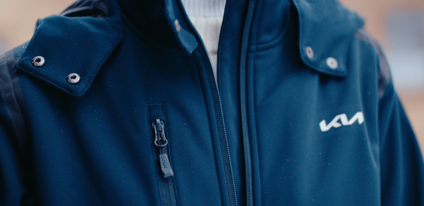 Close-up of a navy blue Kia-branded jacket with snap-button collar details and embroidered logo.