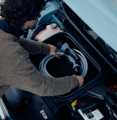 Close-up of a person removing a charging cable from its storage compartment under the hood of an electric vehicle.