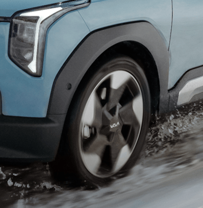 Close-up of a Kia vehicle's front wheel and alloy rim driving through wet, splashing road surface.
