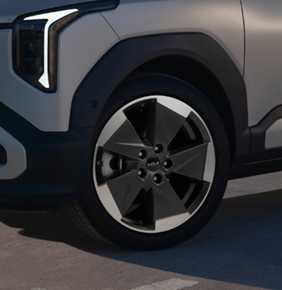 Close-up of a Kia vehicle's front alloy wheel and headlight, parked on pavement.