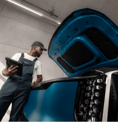 Close-up of a technician performing a vehicle safety check, measuring tread depth on a tire with a gauge during a workshop inspection.