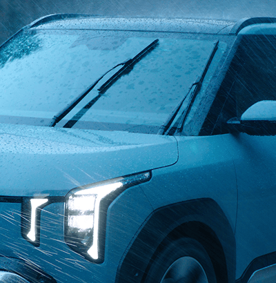 Close-up of a car's front end in heavy rain, with illuminated headlights and windshield wipers in motion.