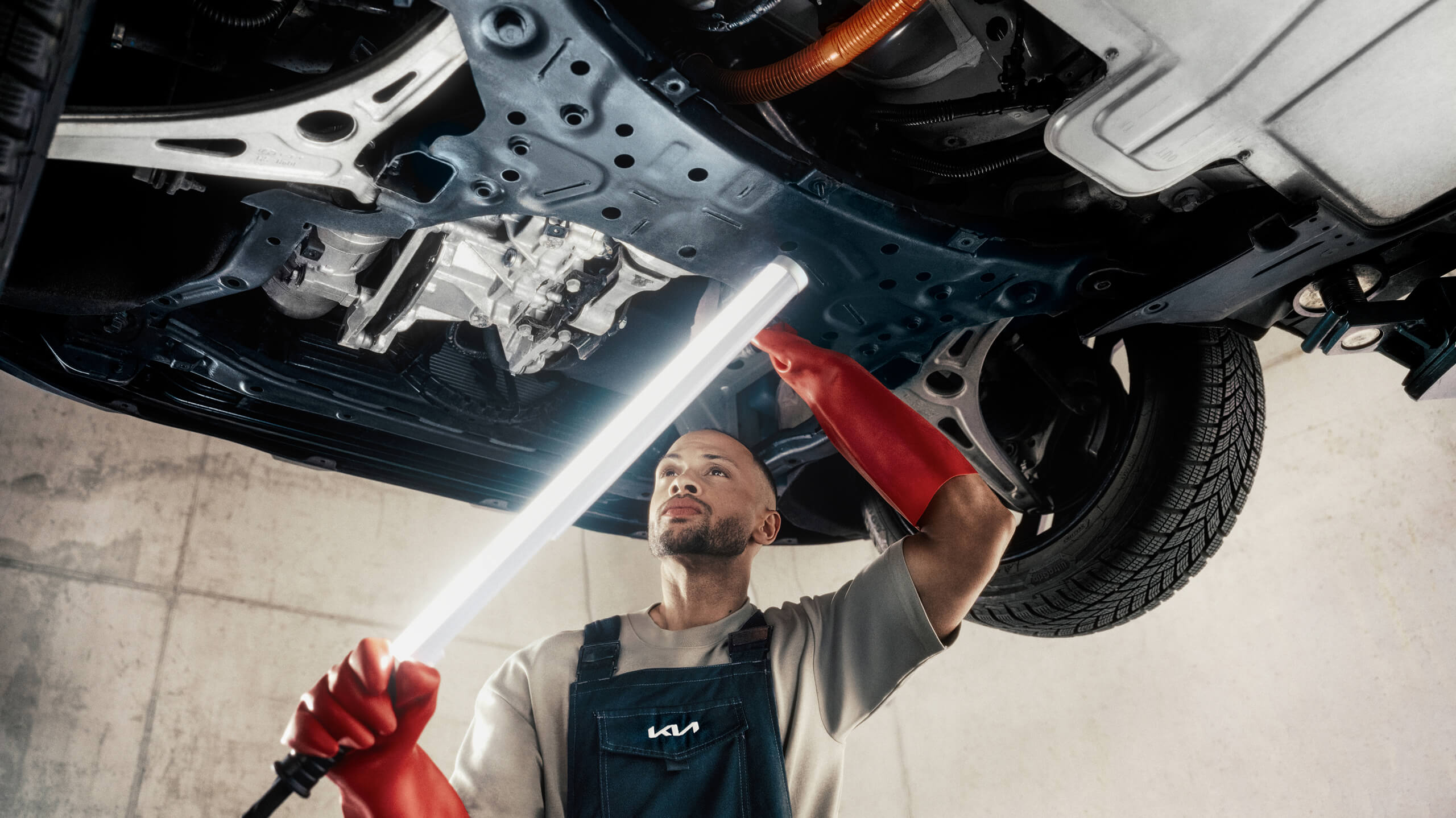 A Kia EV Specialist examines the high-voltage system of a Kia EV3 from underneath.