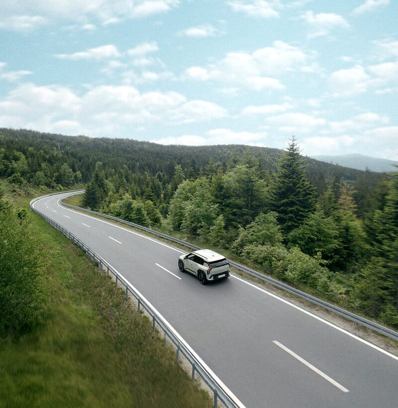 Kia EV3 driving along a scenic forest road toward the horizon.