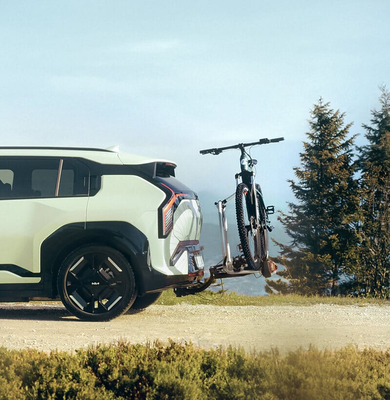 Kia EV3 with Kia Genuine Tow Bar Bike Carrier holding a bicycle in a scenic outdoor setting.