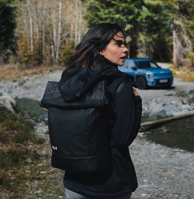Adventurer in Kia Collection gear returns to her Kia EV9 after a nature hike.
