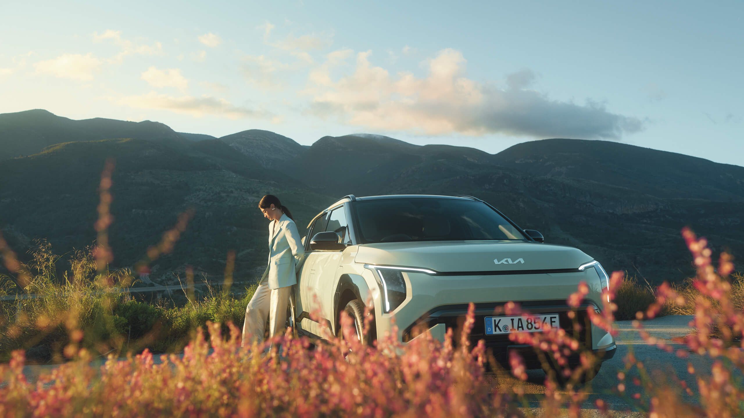 Woman enjoys summer in beautyful mountain setting next to her Kia EV3. 