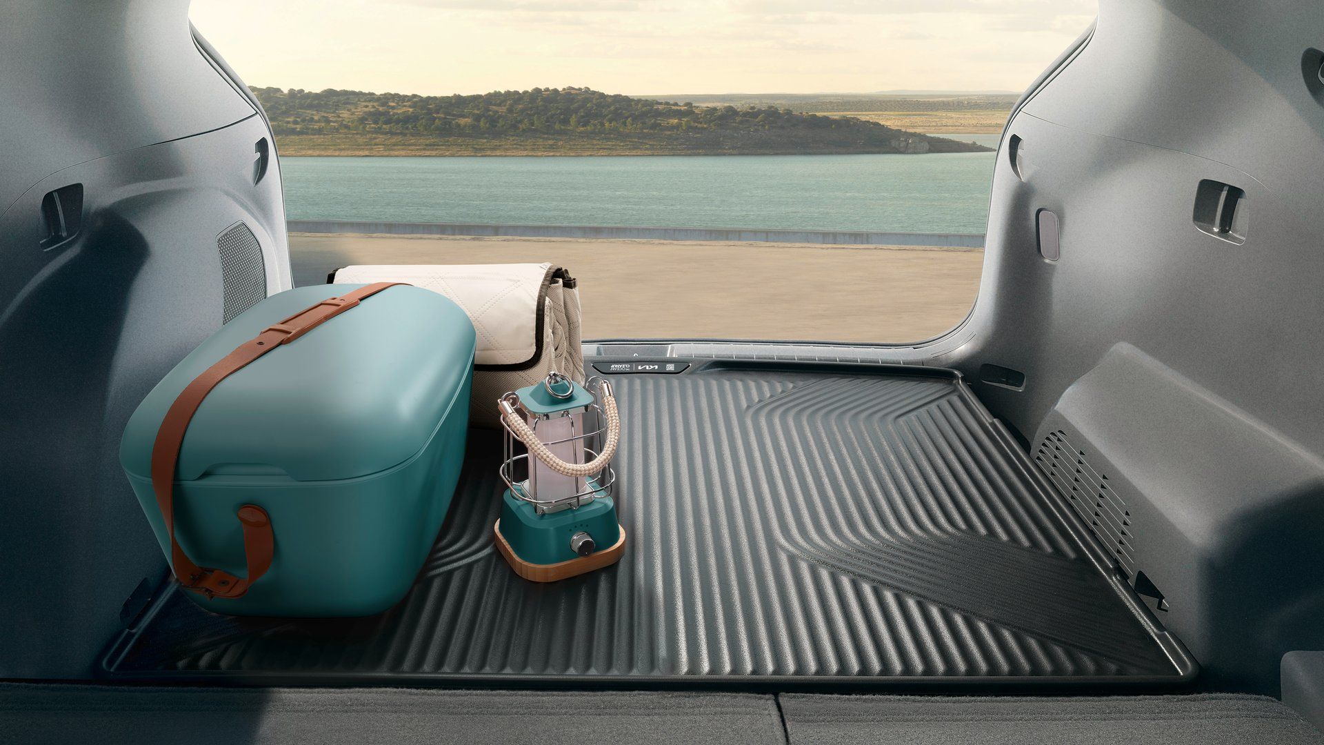 Revestimiento para el maletero del Kia EV3, con una nevera portátil y una linterna, frente al mar