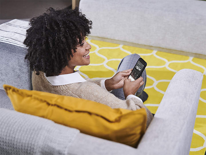 Una mujer sentada en el sofá usando una app de servicios Kia