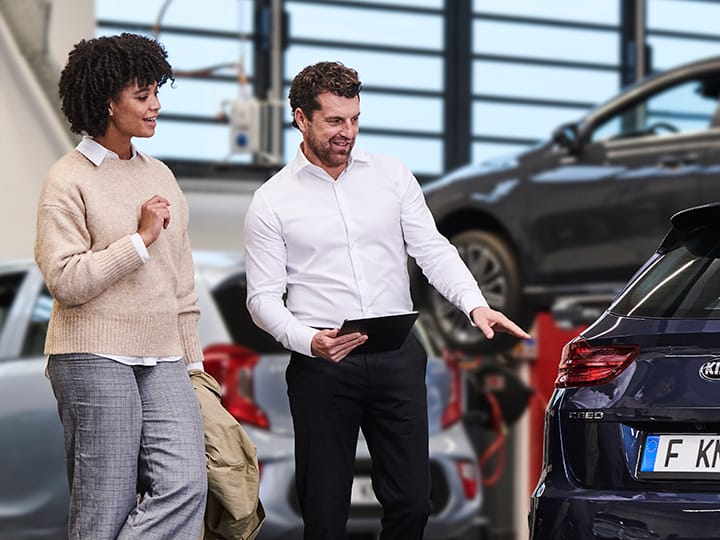 Un mecánico muestra a una clienta una pieza original de Kia