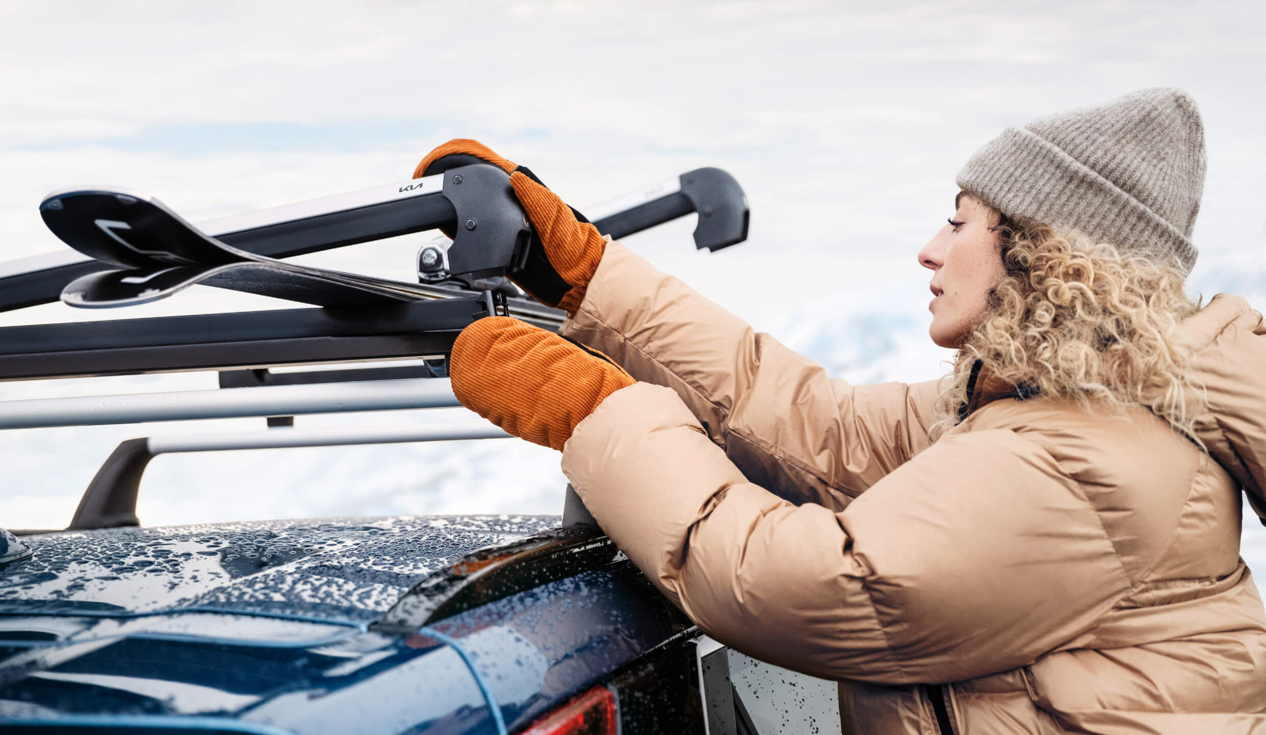 Woman in winter clothing takes skis from the Kia Ski and Snowboard Carrier.