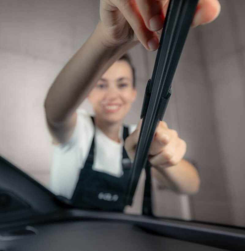 Female Kia technician replaces wiper blades for clear winter visibility.