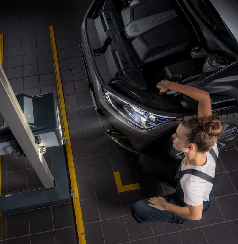 Female Kia technician tests and adjusts the LED lights of a Kia with a headlight aiming device.