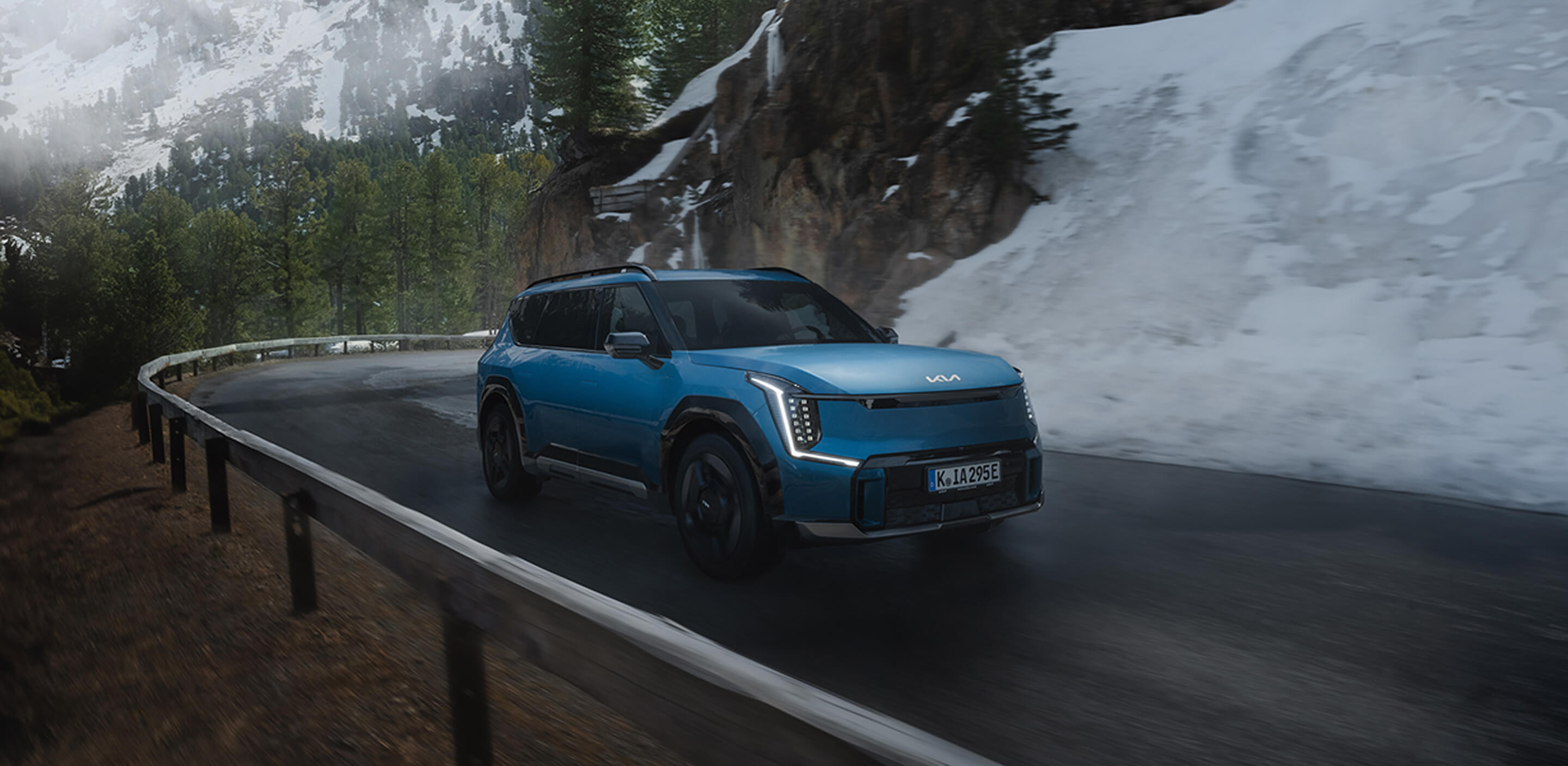 Kia EV9 navigates a steep curve on a wintery mountain road with safety and control.