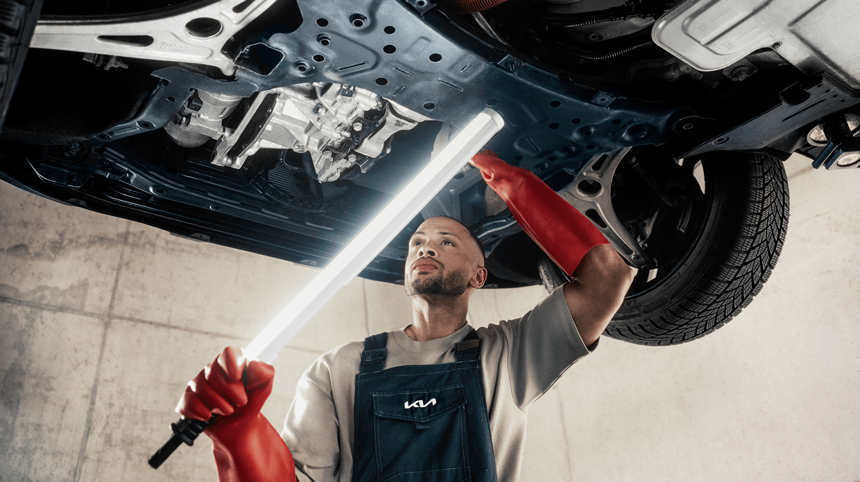 Professional technician examining Kia undercarriage as part of comprehensive Vehicle Health Check.