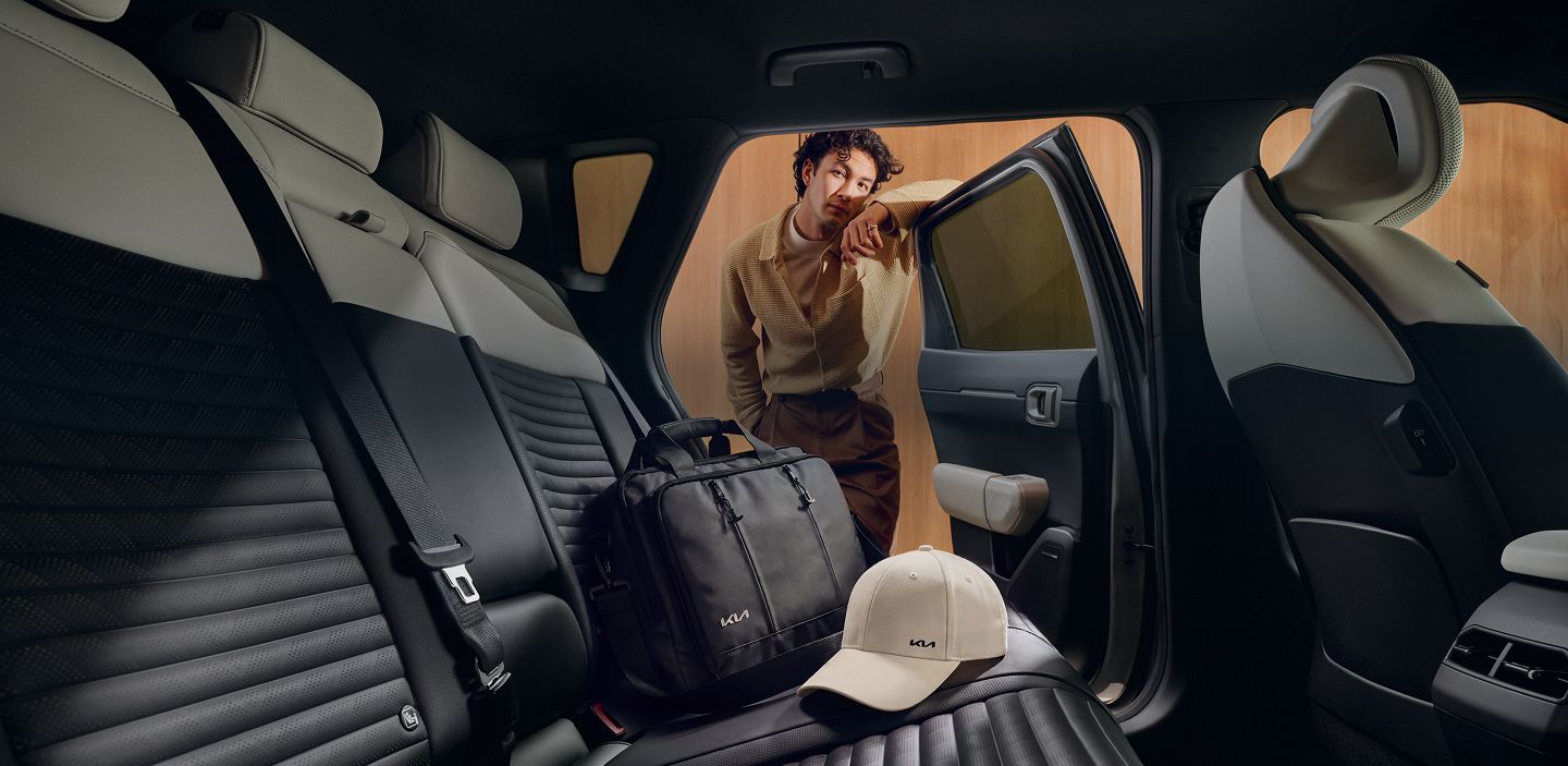 Man placing a Kia Laptop Bag and Kia Sports Cap on the rear seats of his Kia EV4.