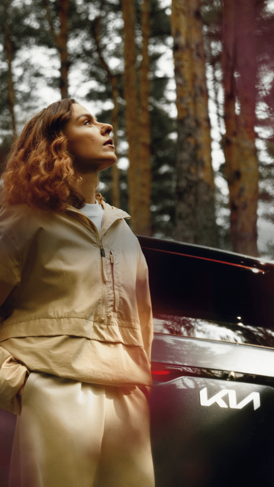 Woman enjoying the fresh summer air beside her Kia EV5.