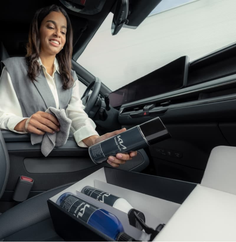 Woman is cleaning the cabin of her Kia with the Kia Car Care Set.