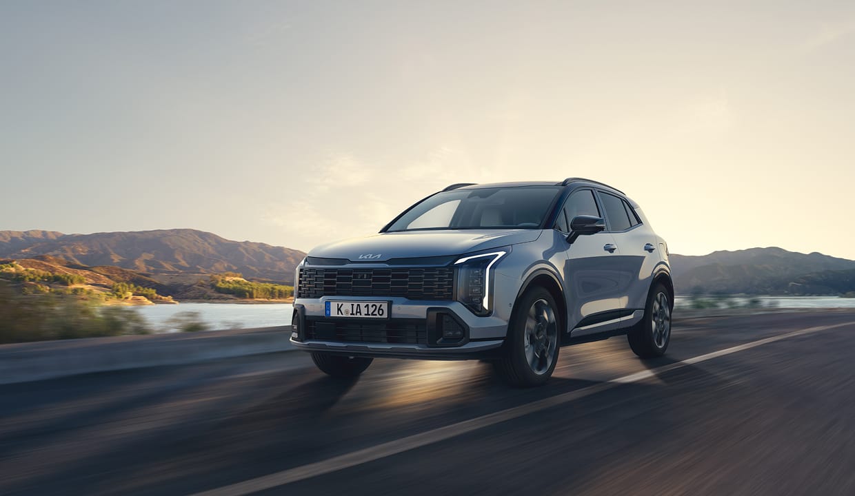 A Kia Sportage drives along an open road on a bright summer day.