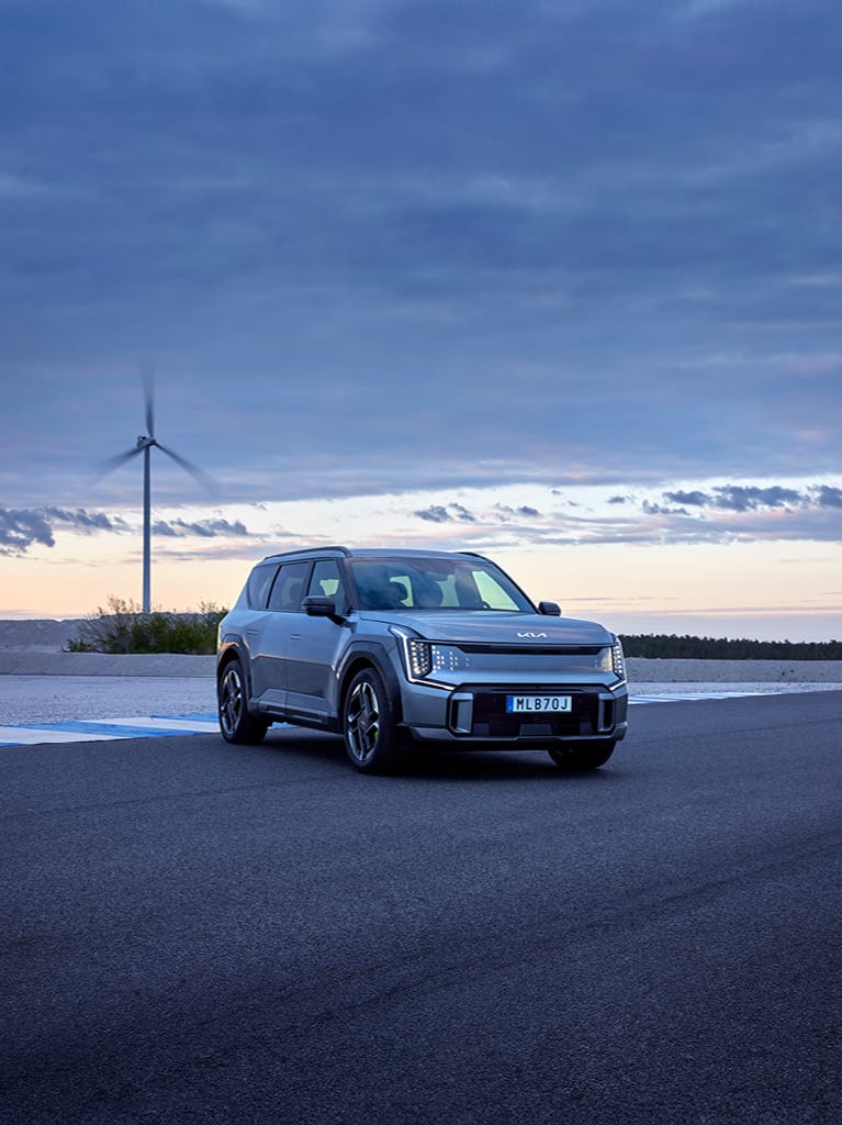 Helelektriska Kia EV9 GT sedd snett framifrån på en racingbana i solnedgången.