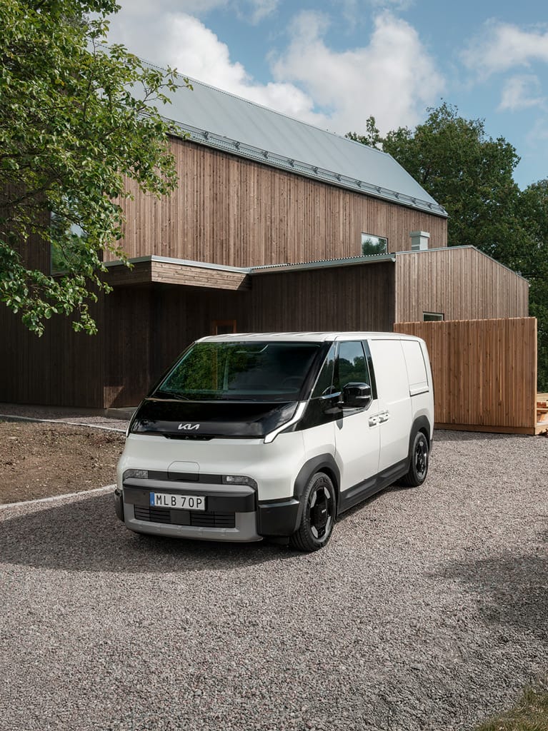 Kias transportbil Kia PV5 Cargo i vitt utförande framför ett modernt hus.