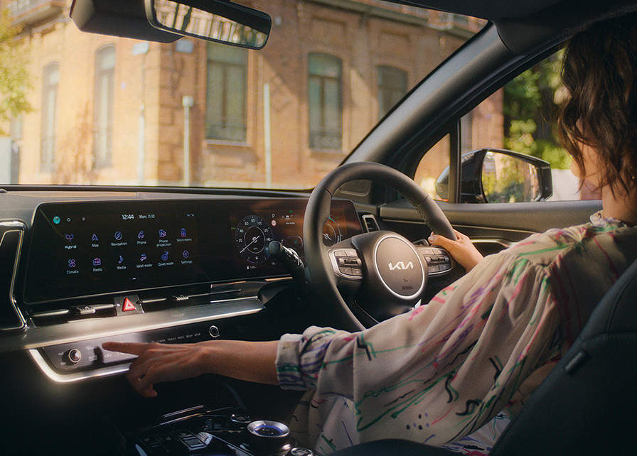 woman driving a Kia and enjoying the in-car technology.  Including Kia Connect in-car services.