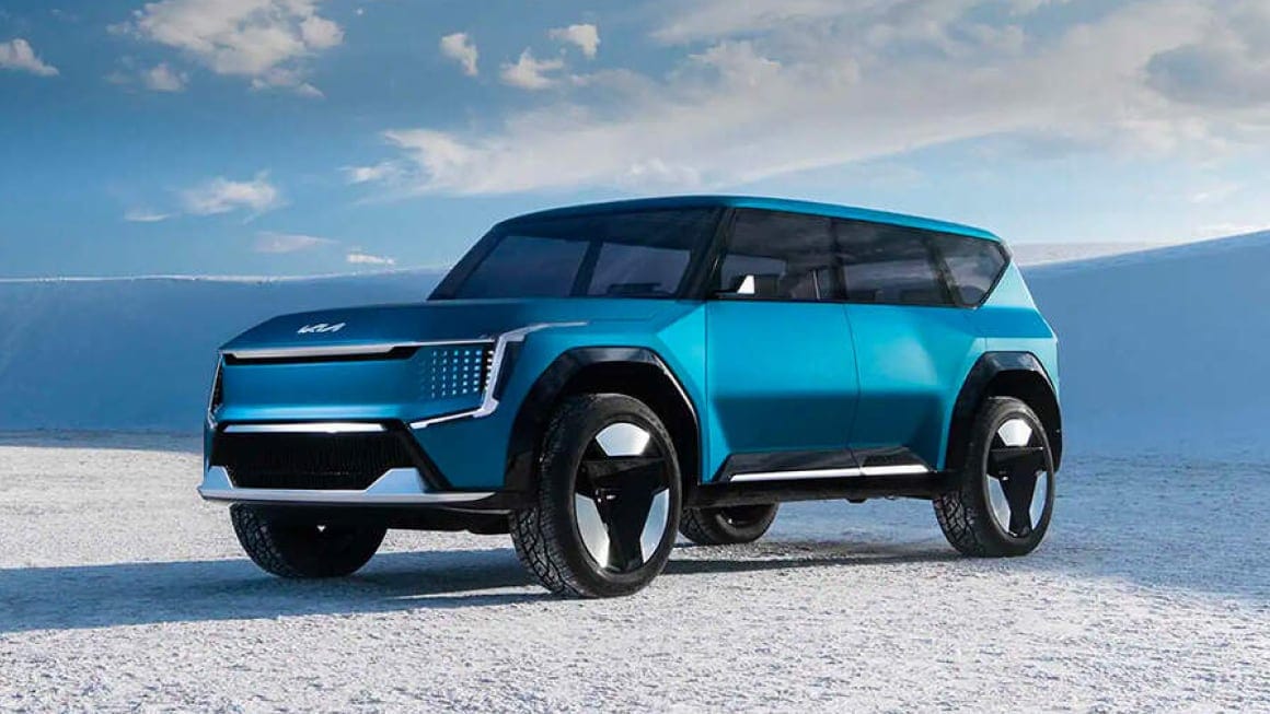 The Kia EV9 driving on a road through a countryside landscape.