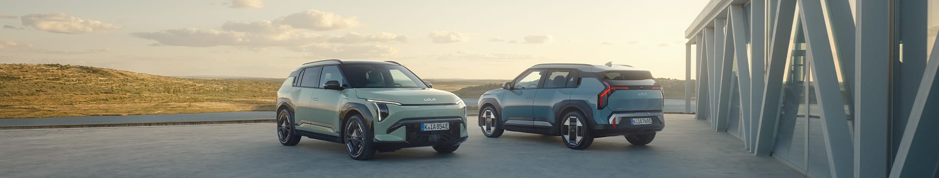 The Kia GT-Line S EV6 in Wolf Grey driving across a modern bridge, with a sunset in the background.