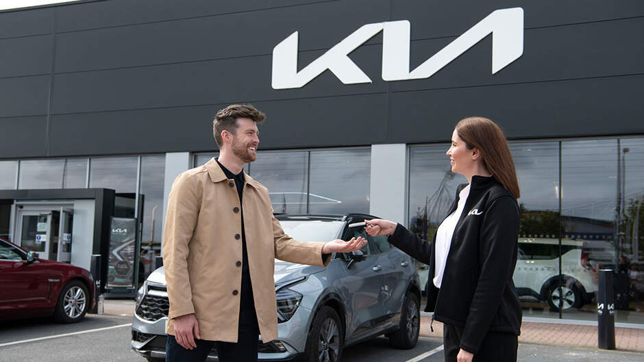 Kia dealer and customer shaking hands outside dealership