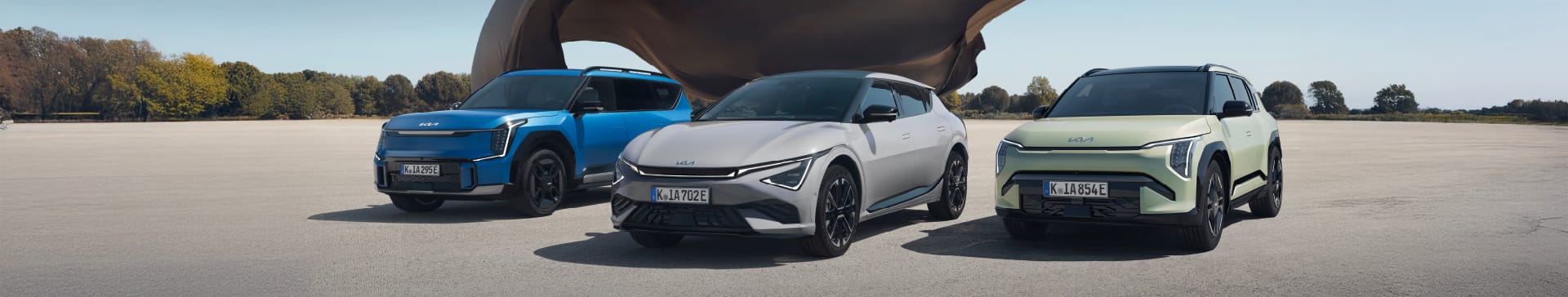 A side profile of the Kia GT-Line S EV6 in Wolf Grey, with a man sat in the passenger seat his legs out of the car. The EV is parked in an area with stones on the floor, and cylindrical cooper panelled building behind.
