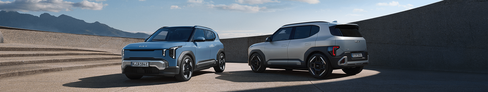 Two Kia EV2's parked near stairs with a mountain in the background