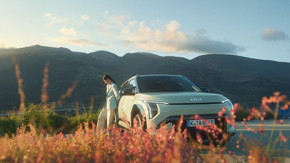 Front of green Kia EV6 with model in front kicking a can