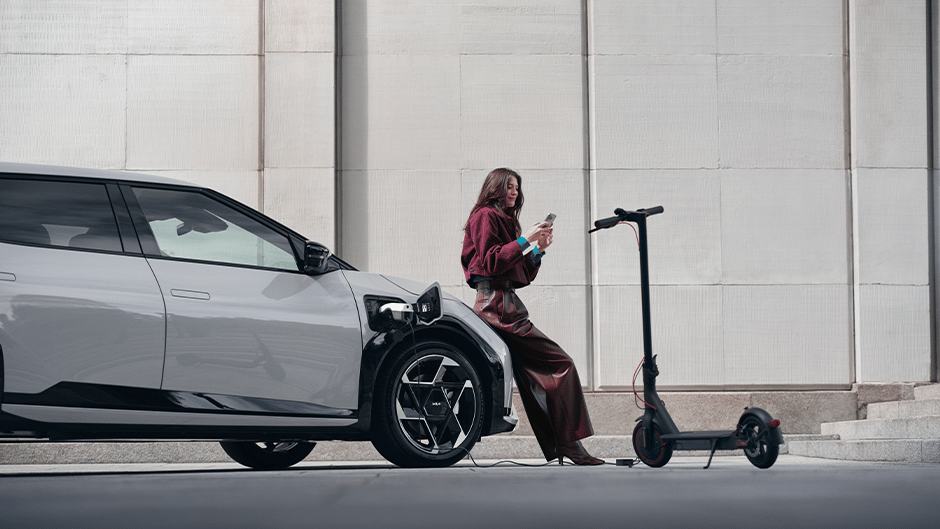The Kia EV4 in Wolf Grey charging a scooter