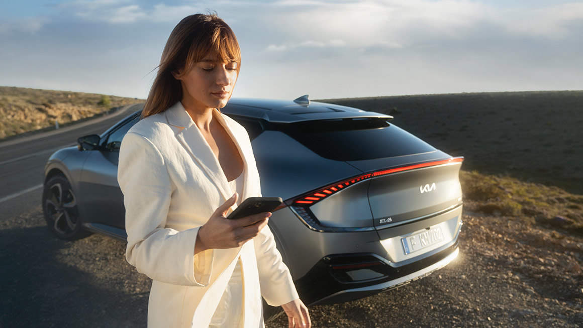 A woman standing by an EV6 parked on a hill