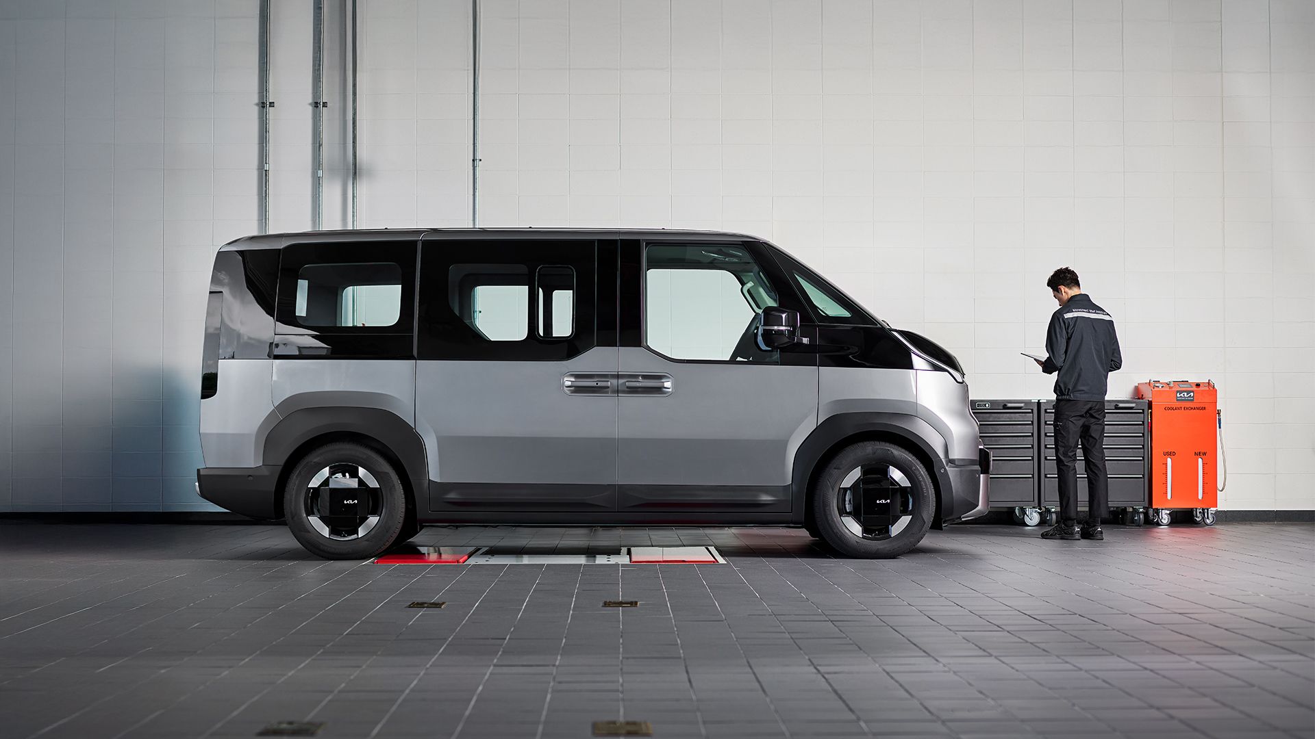 Side view of the Kia PV5 in a service bay with a technician working at a tool chest