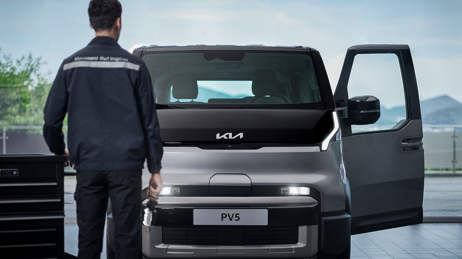 Technician standing in front of the Kia PV5 in a service bay with the driver’s door open