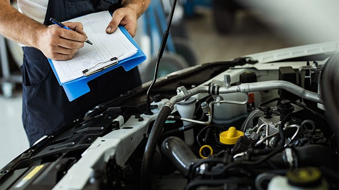 Mechanic is checking the inspection list in front of a open bonnet 