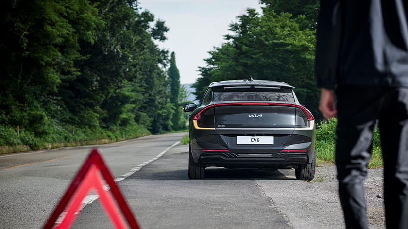 Kia Roadside Assistance technician approaching a stopped Kia EV6 on a rural road